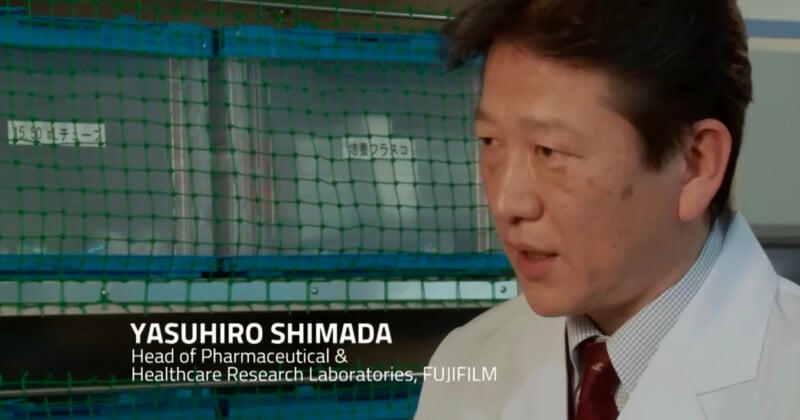 A man in a white lab coat, identified as Yasuhiro Shimada of Fujifilm’s Healthcare Research Laboratories, speaks in a laboratory setting with green storage racks in the background.