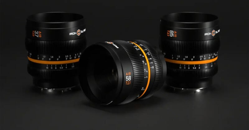 Three black camera lenses with orange accents are displayed on a dark surface; two stand upright in the background, and one lies horizontally in the front, showing the "58 T2.1" marking.