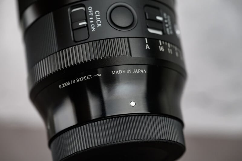 Close-up photo of a black camera lens showing detailed focus and mode switches, a focus distance marking of 0.28m/0.92 feet to infinity, and the words "MADE IN JAPAN" engraved on the lens barrel.
