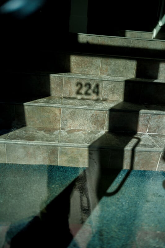 Sunlight casts shadows on tiled steps, with the number "224" clearly visible on the middle step. A blurry reflection and handrail are seen in the foreground.