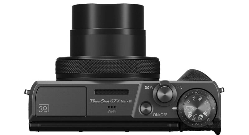Top view of a black Canon PowerShot G7 X Mark II digital camera with an extended lens, control dial, shutter button, on/off switch, and Wi-Fi marking visible.