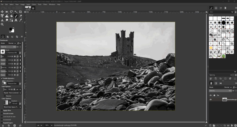 A black and white photo of a rocky landscape with an old, ruined stone tower on a hill, shown open for editing in GIMP software, with toolbars and panels visible around the image.
