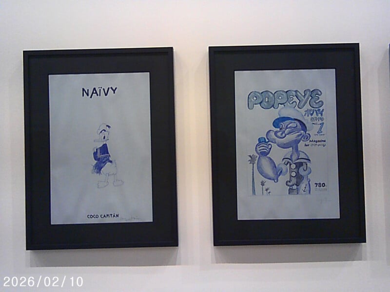 Two framed drawings on a wall: one shows Donald Duck with the text "NAÏVY" above him, the other features Popeye with the text "POPEYE" and additional magazine-like text. The artwork is mostly in blue and gray tones.