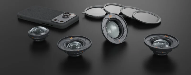 A smartphone with a textured case is surrounded by three detachable camera lenses and several circular lens filters on a dark surface, showcasing mobile photography accessories.
