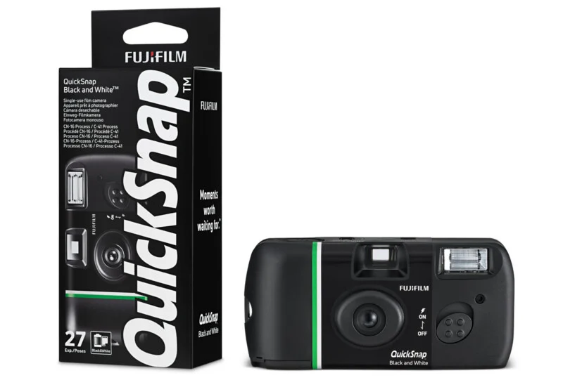 A Fujifilm QuickSnap Black and White disposable camera is shown next to its black packaging box. The camera has a green stripe and built-in flash. The box displays product details and the number 27 for exposures.