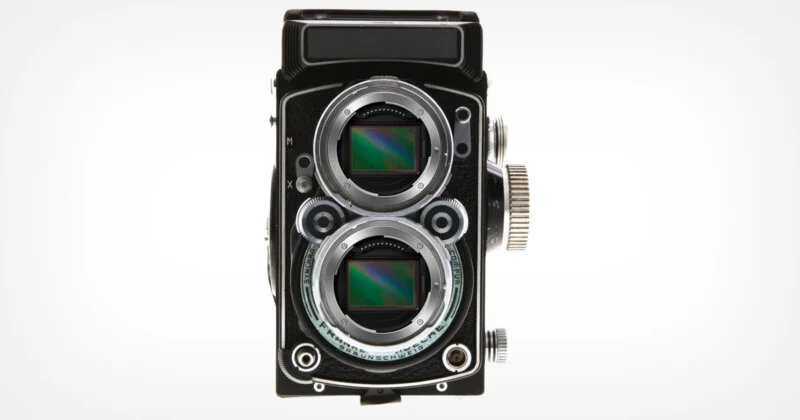 A vintage twin-lens reflex camera with modern digital sensors visible in both lens openings, set against a plain white background.