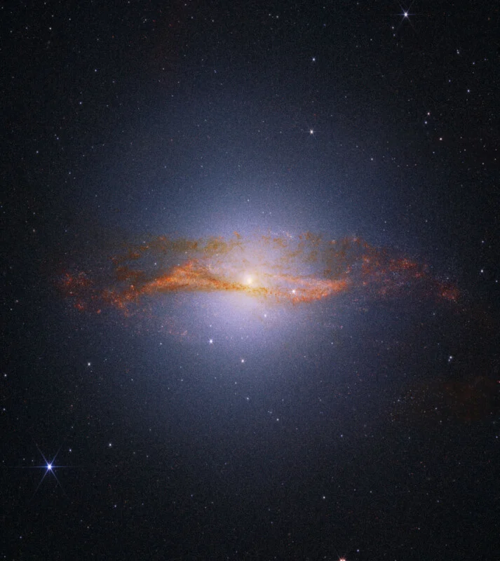 A bright spiral galaxy with a glowing center and orange-tinted dust lanes, surrounded by a dark star-filled space background.