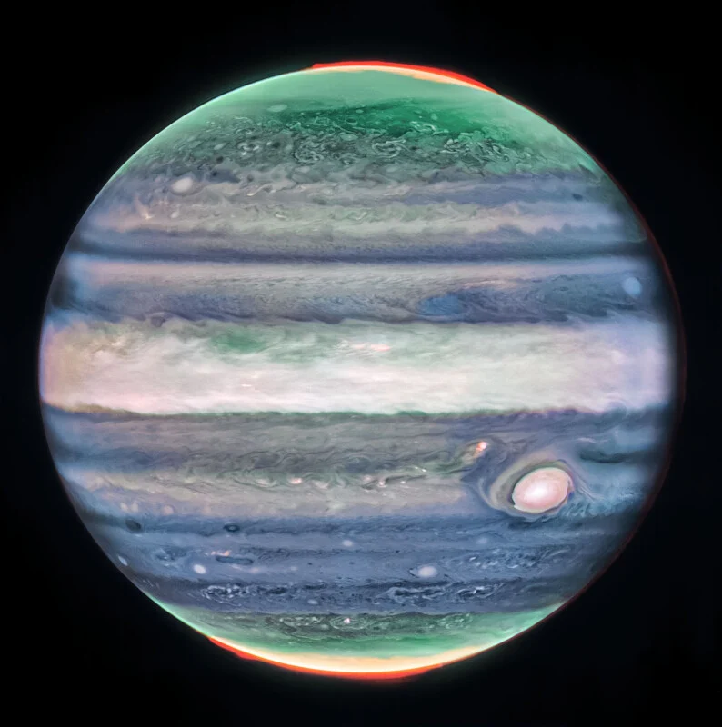 Image of Jupiter with colorful bands, showing green and red hues near the poles, and the Great Red Spot visible on the lower right. The planet appears vibrant against a black background.