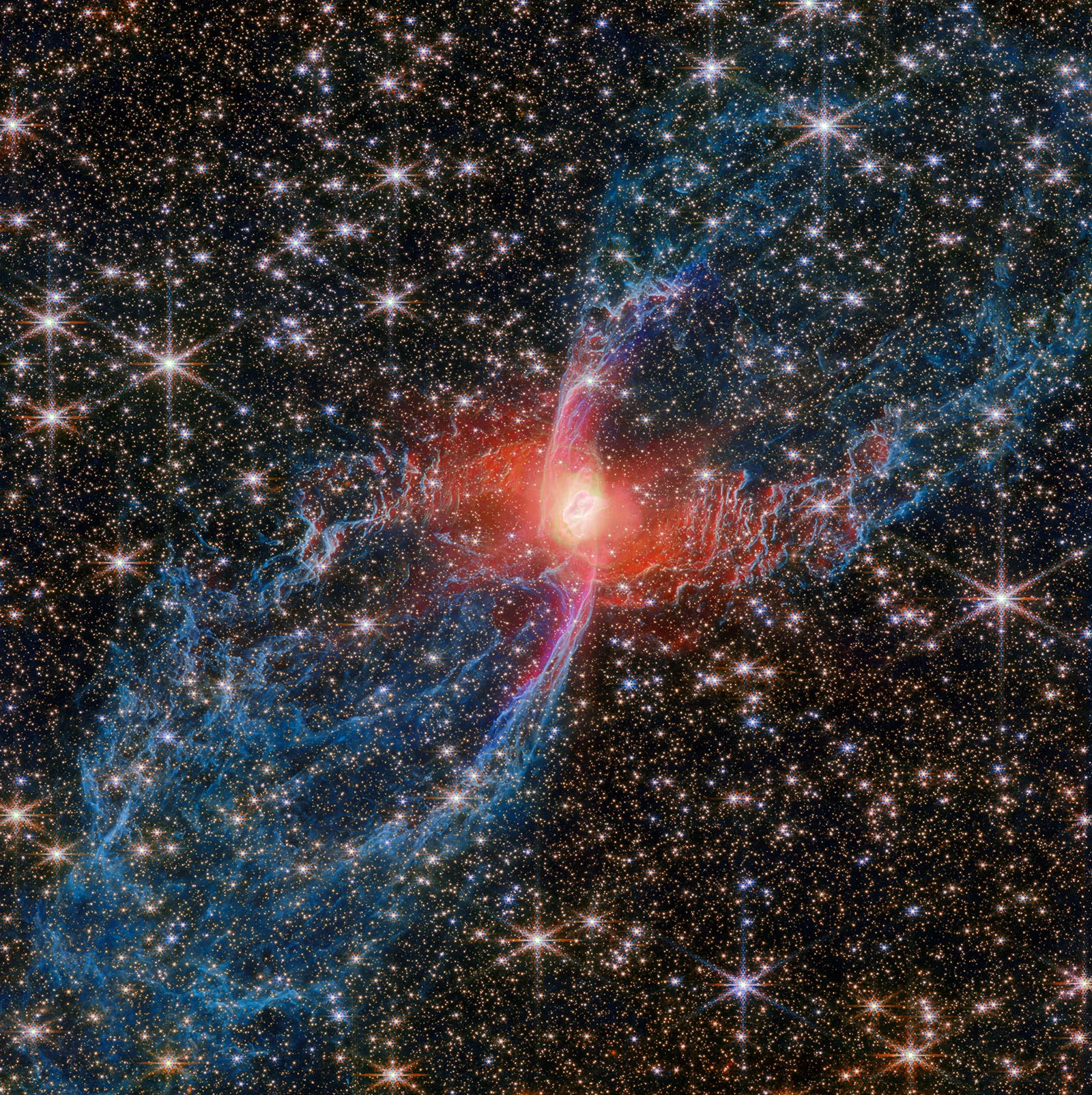 Colorful nebula with a bright red center, surrounded by blue and pink wispy clouds and many sparkling stars scattered throughout the dark space background.