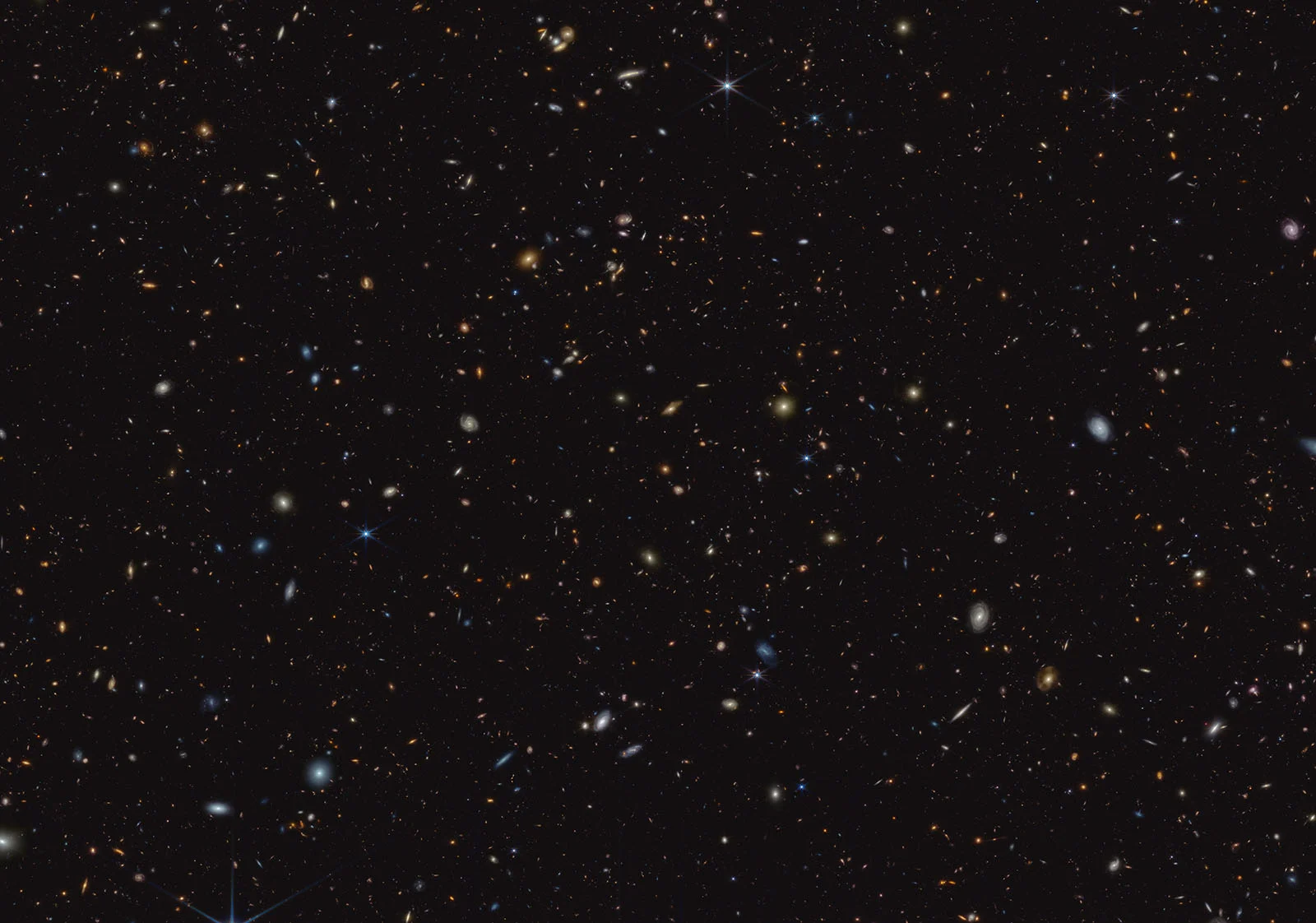 A deep space image showing countless distant galaxies, stars, and cosmic objects scattered across a dark, star-filled background.