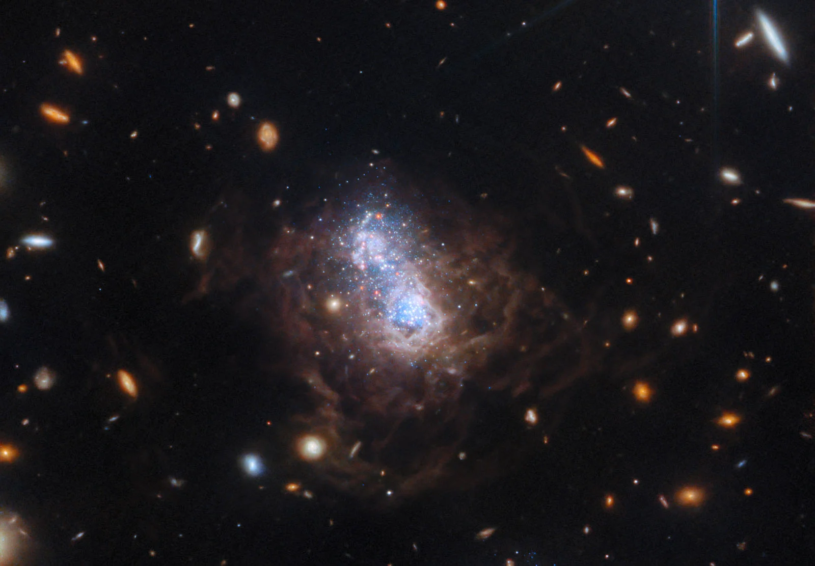 A bright blue galaxy glows at the center, surrounded by swirling clouds of dust and distant, scattered stars and galaxies against the dark backdrop of space.