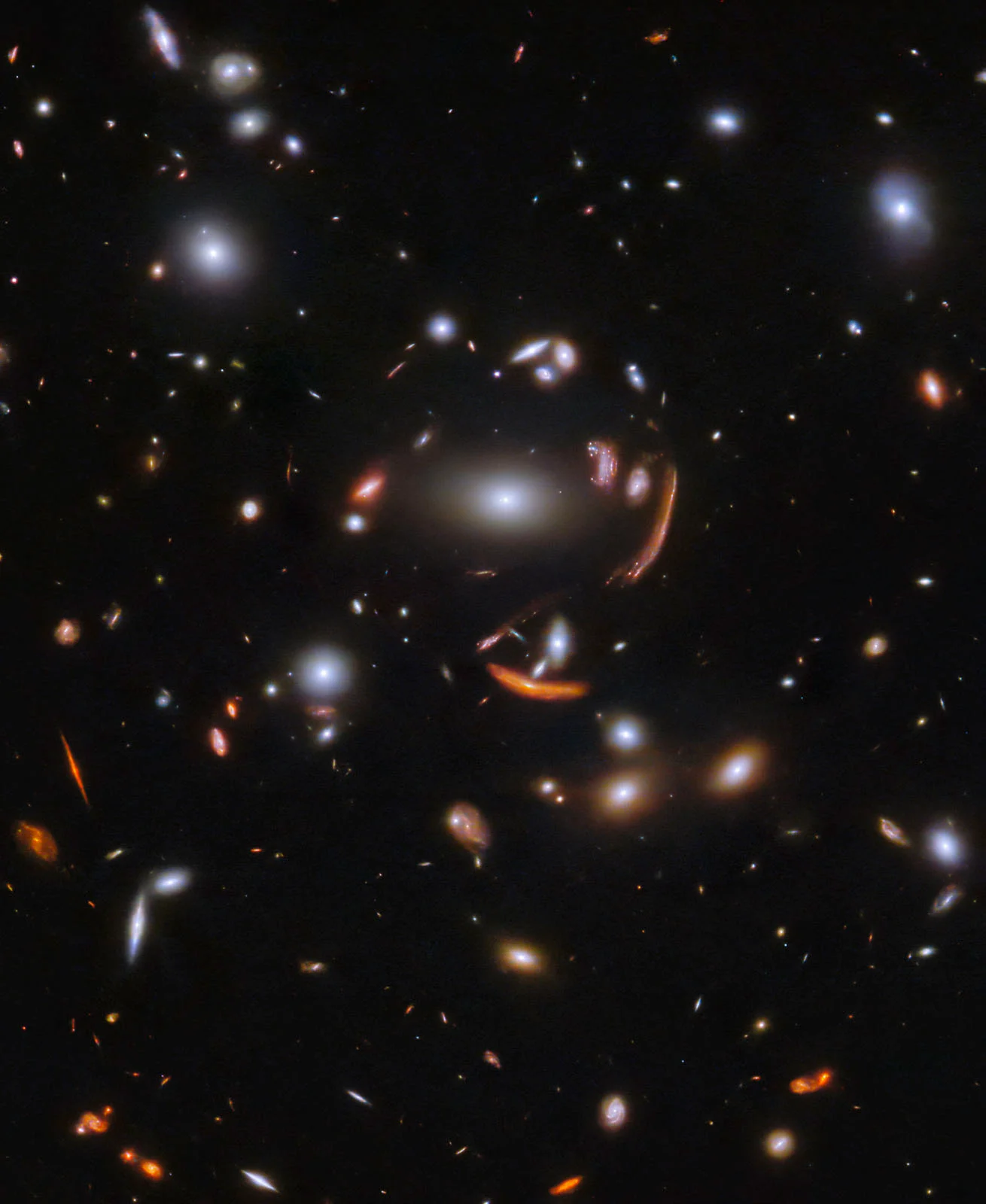 A deep space image shows numerous bright galaxies of various sizes and shapes against a dark background, with some galaxies stretched into arcs due to gravitational lensing.