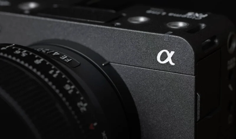 Close-up of a black Sony Alpha series camera, showing its textured body, lens details, and the white Alpha (α) logo on the front corner.