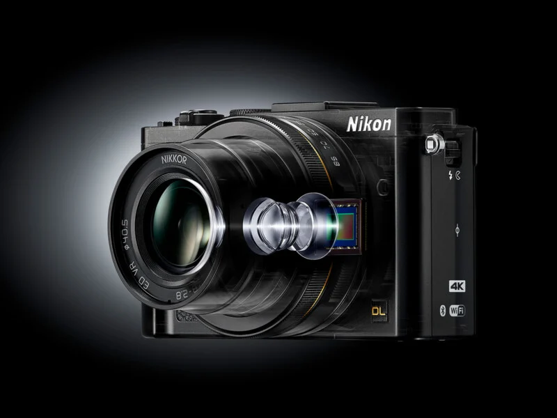 A black Nikon digital camera with a visible lens assembly and image sensor, showing the internal components in a semi-transparent, exploded view style.