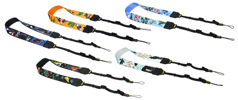Five colorful camera neck straps are arranged on a white background, each featuring unique artistic patterns including birds, fish, and botanical motifs, equipped with adjustable black nylon webbing and attachment loops.
