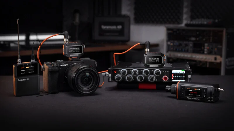 A professional audio setup featuring Saramonic timecode generators, a Sony camera, and a multi-channel field recorder on a table.