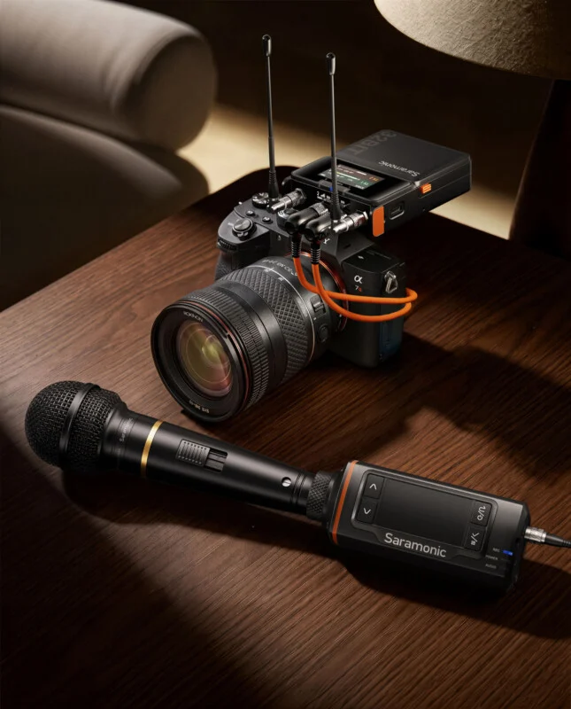 A Saramonic wireless microphone receiver is mounted on top of a camera, with a handheld Saramonic microphone lying on a wooden table in the foreground.
