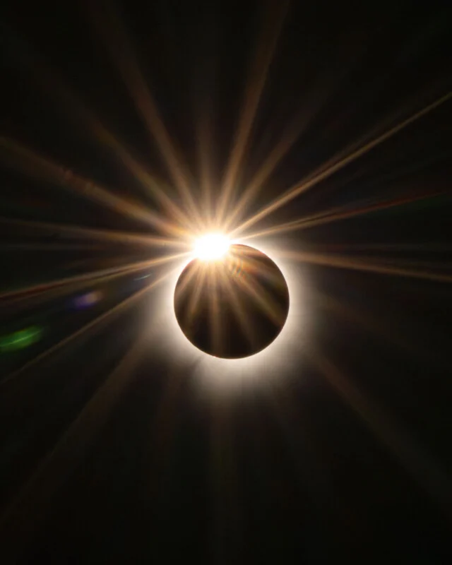 A total solar eclipse showing the moon silhouetted against the sun, creating a bright diamond ring effect with radiating light.
