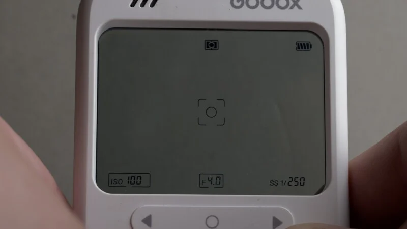 A close-up of a white digital device screen displaying camera settings: ISO 100, F4.0, and SS 1/250, with a central focus bracket icon.