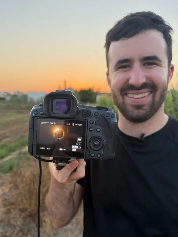 Een glimlachende man houdt een camera voor zich, terwijl hij een foto van een zonsverduistering op het digitale scherm toont.
