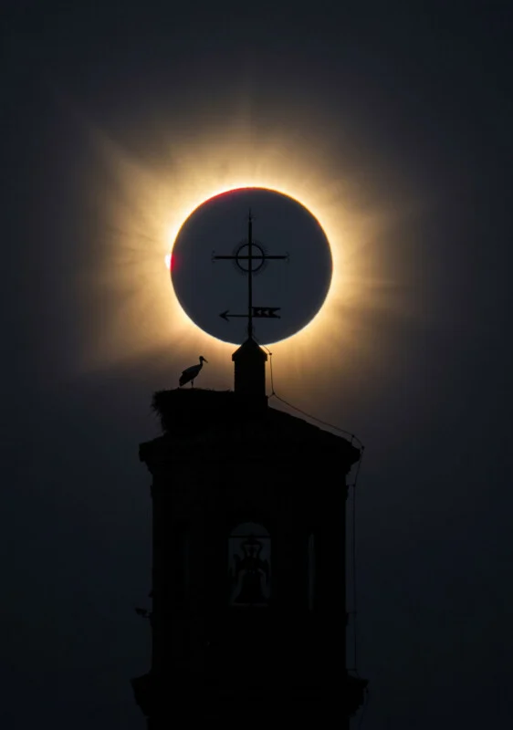 Zonsverduistering verschijnt direct achter de kruisvormige spits van een klokkentoren, waar een ooievaar in een nest staat.