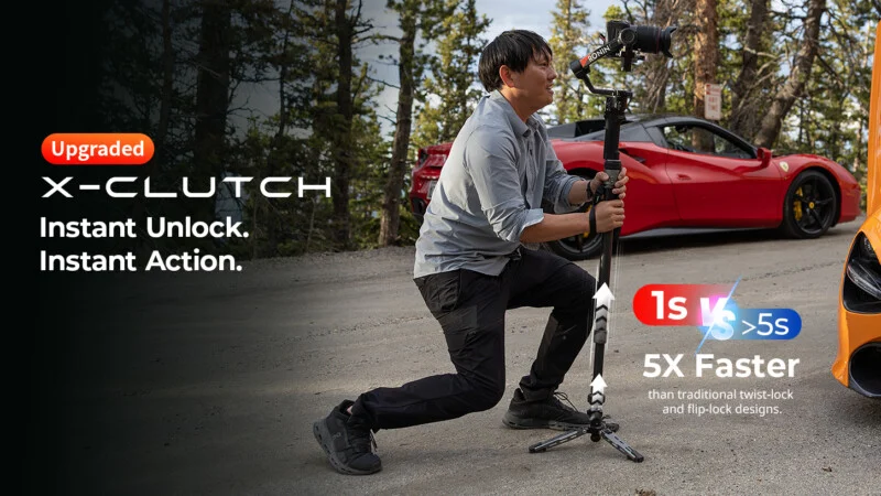 A person in a light shirt and dark pants kneels on a road while holding a camera stabilizer, with a red sports car parked in the background.