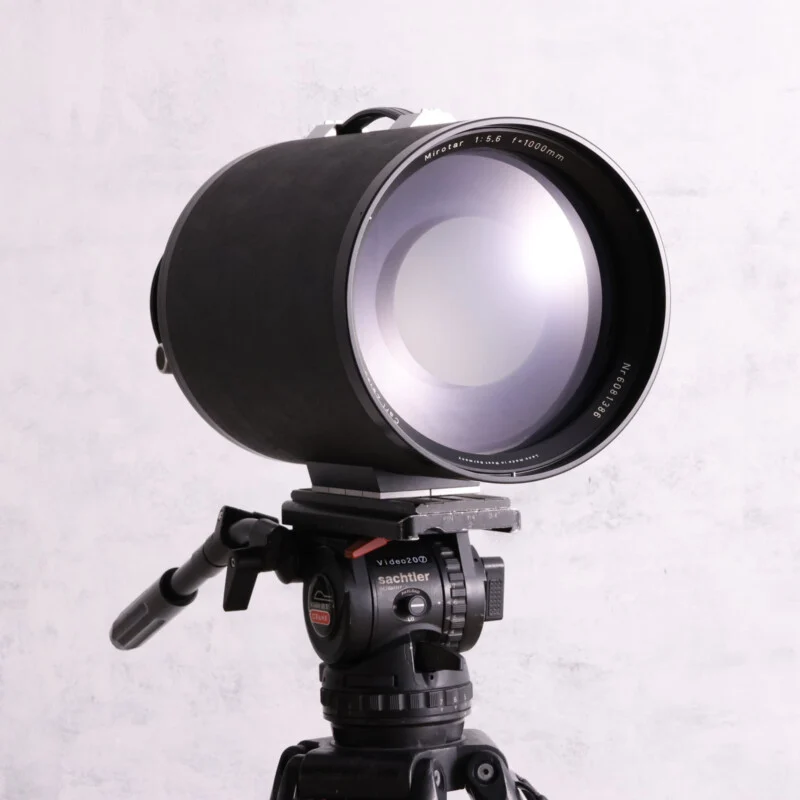 A large Carl Zeiss Mirotar 1000mm f/5.6 telephoto lens mounted on a Sachtler Video 20 tripod head against a light gray background.