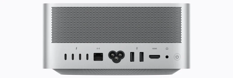 The back panel of a silver computer features a large ventilation grille above a row of ports, including four Thunderbolt ports, an Ethernet port, a power input, two USB-A ports, an HDMI port, a headphone jack, and a power button.