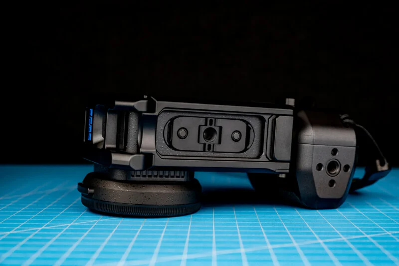 A black camera accessory with a lens cap rests on a blue grid cutting mat against a black background.