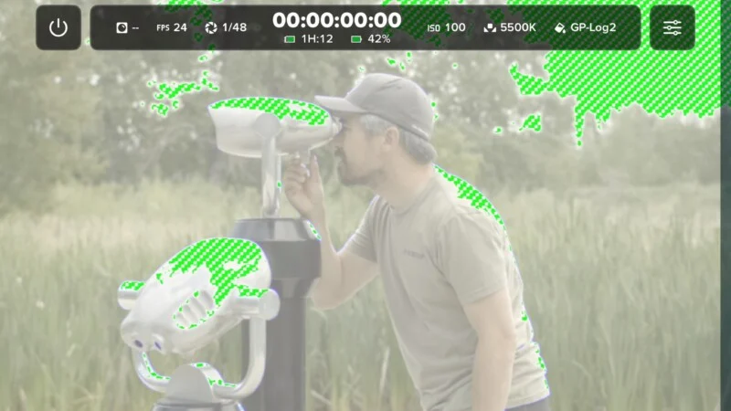 Een man kijkt door een staand publiek verrekijker in een groen veld met groene zebra-Exposure-waarschuwingen op de heldere delen van het beeld.