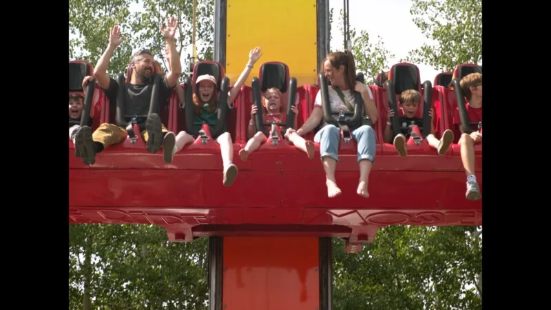 Een groep kinderen en volwassenen die achter een rode valtoren- attractie zitten met hun armen omhoog.