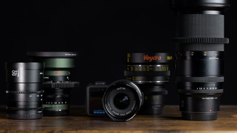 Een verzameling verschillende cameralenzen en een GoPro-camera op een houten oppervlak tegen een zwarte achtergrond.