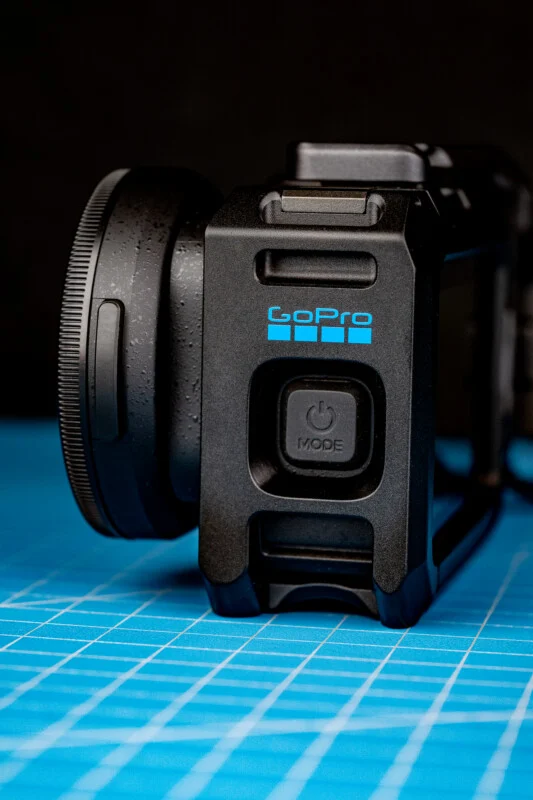 Een zwarte GoPro-behuizing met een aan/uit-knop ligt op een blauwe rastersnijmat tegen een donkere achtergrond.