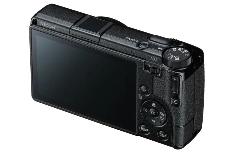 A black Ricoh digital camera viewed from the rear, showing the LCD screen, mode dial, and various control buttons.