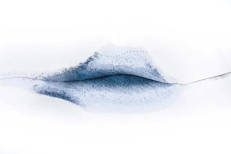 A dark, horizontal crack runs through a patch of blue-tinted snow against a stark white background, resembling the shape of lips.