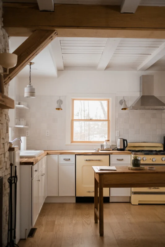 A kitchen features white cabinets, a pale yellow dishwasher and stove, a wooden countertop, and a wooden table in the center.
