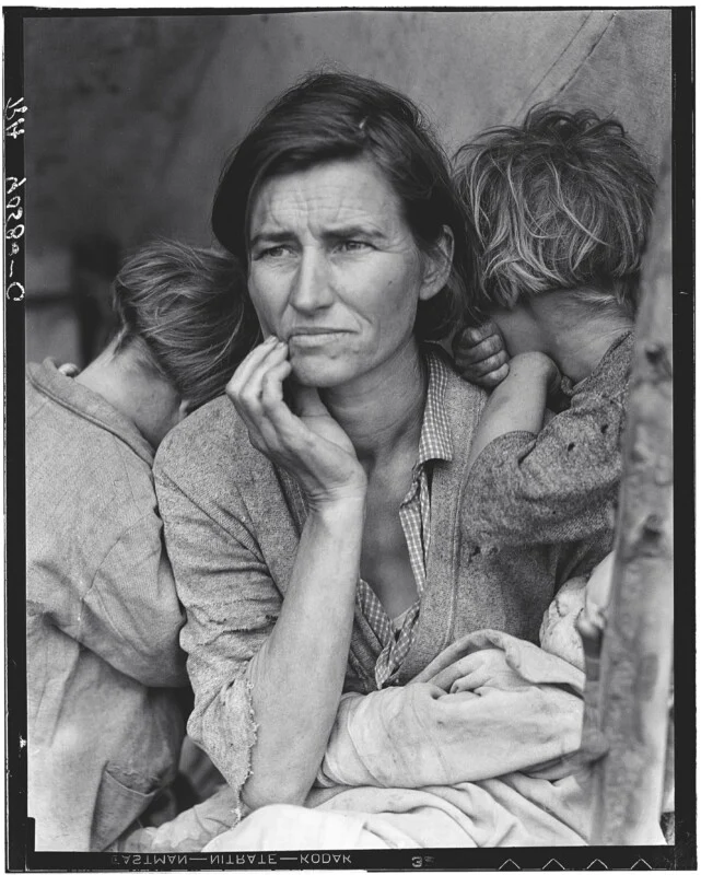 A woman with a worried expression rests her chin on her hand, surrounded by three young children who are leaning against her.
