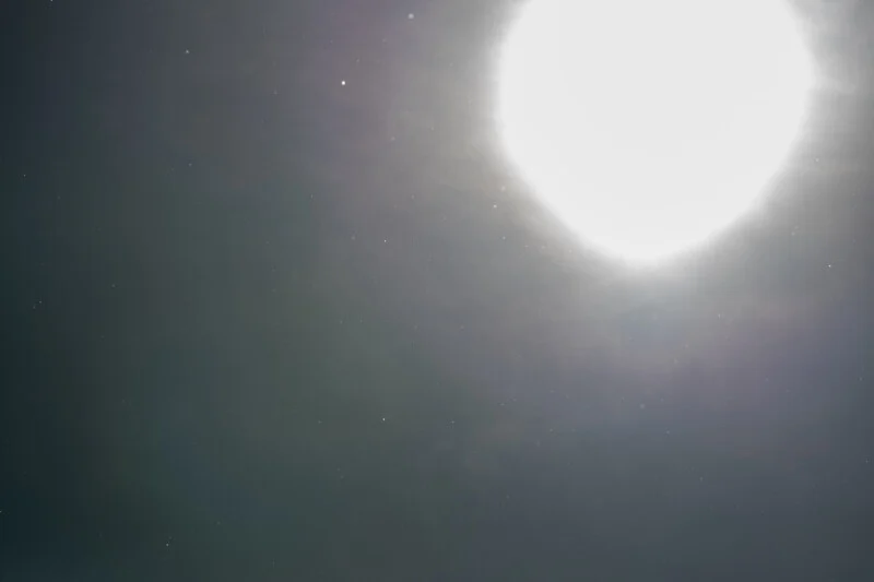 A bright, glowing sun shines in the upper right corner of a dark, hazy sky filled with scattered dust particles.