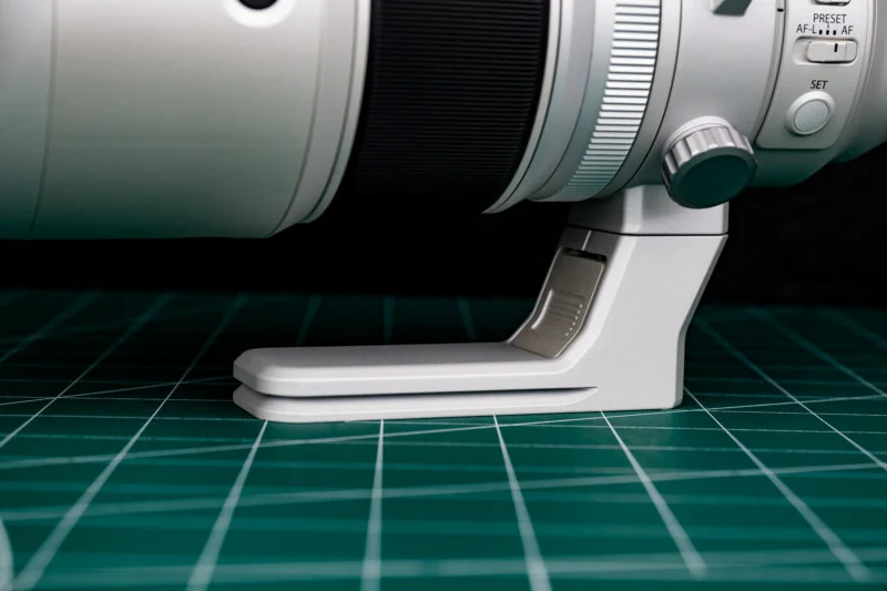 A close-up of a white camera lens tripod foot resting on a green cutting mat with white grid lines.