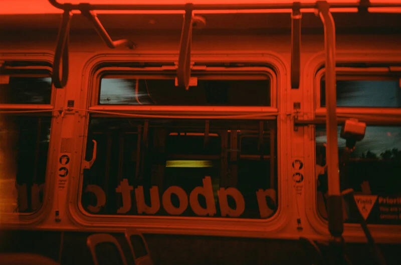 The interior of a bus bathed in red light, showing windows with reversed text and handrails.
