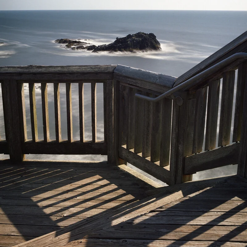 A wooden deck with railings overlooks a calm ocean with a rocky island in the distance.
