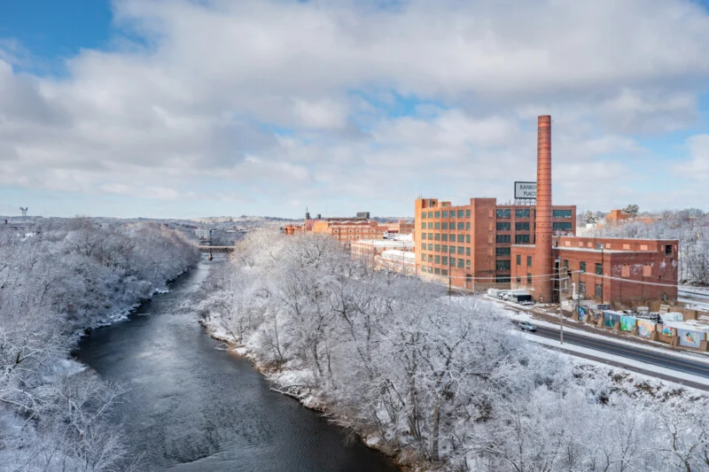 A river flows past snow-covered trees and a large brick industrial complex with a tall smokestack labeled Banbury Place.