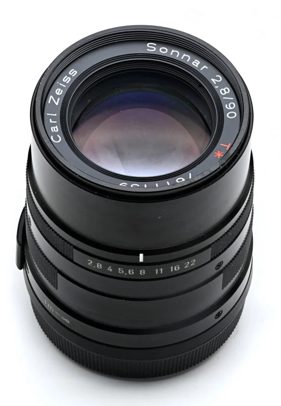 A black Carl Zeiss Sonnar 2.8/90 T* camera lens stands vertically against a white background.