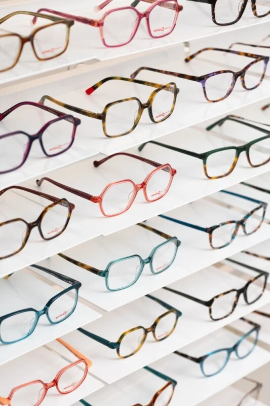 A display shelf filled with numerous pairs of colorful, modern eyeglasses arranged in rows.