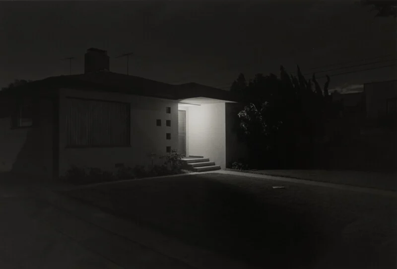 A single-story house at night with a brightly lit entryway contrasting against the dark, shadowed exterior.