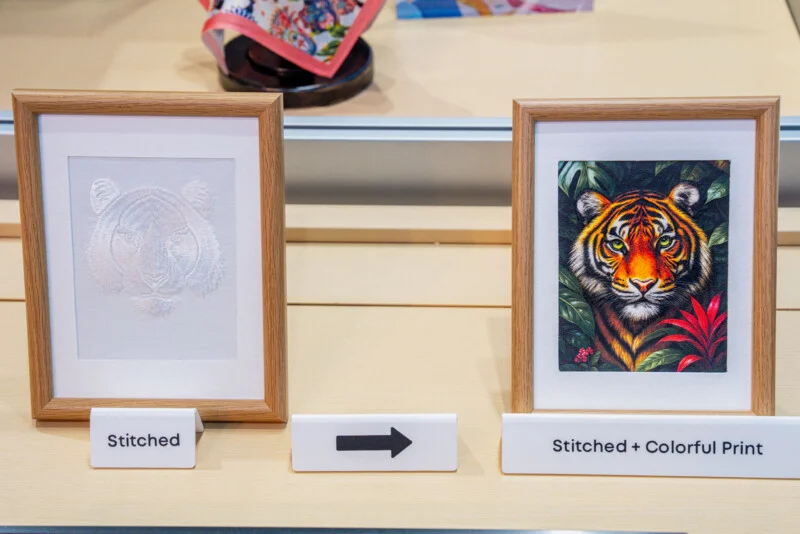 Two framed tiger portraits sit on a light-colored surface, with a label reading "Stitched" under the left one and "Stitched + Colorful Print" under the right one, separated by an arrow.