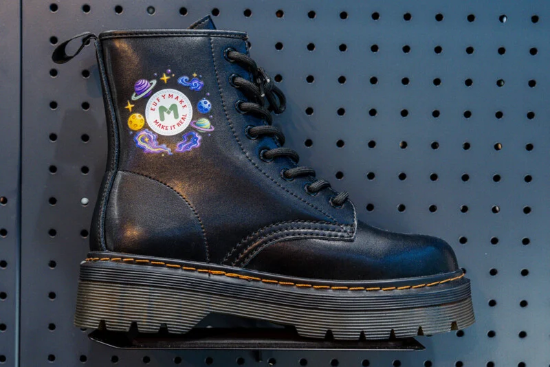A black platform combat boot with yellow stitching sits on a shelf against a dark gray pegboard wall, featuring a circular "EUFYMAKE MAKE IT REAL" logo surrounded by space-themed illustrations.