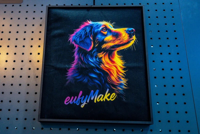 A framed, colorful digital art print of a dog in profile against a black background, with the text "eufyMake" below it, mounted on a dark pegboard wall.