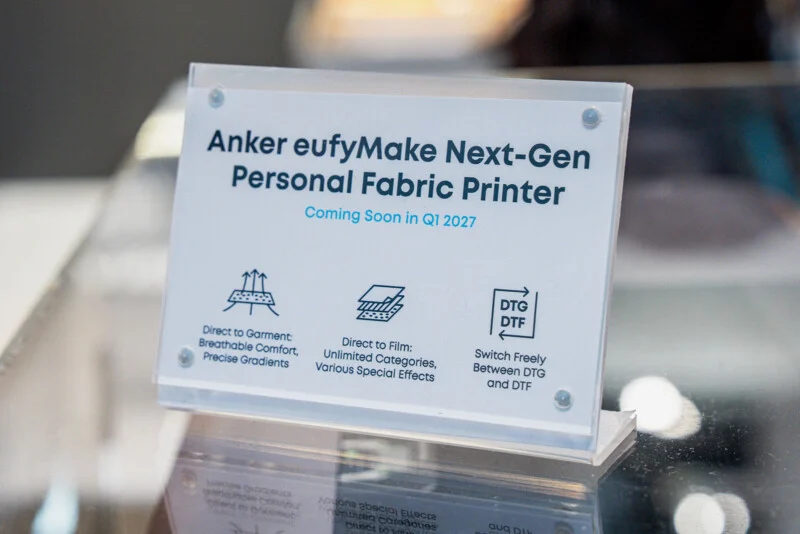 A sign on a stand reads "Anker eufyMake Next-Gen Personal Fabric Printer" with a release date of Q1 2027 and printing features.