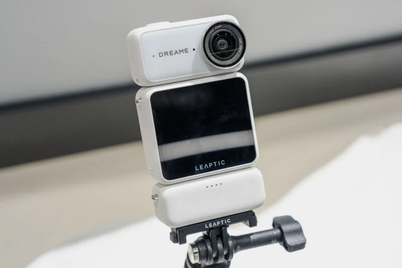 A white, modular action camera with a screen labeled "LEAPTIC" is mounted on a tripod stand against a plain background.